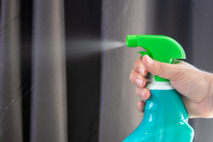 A person spraying cleaning solution into the air with a blue bottle and green nozzle head.
